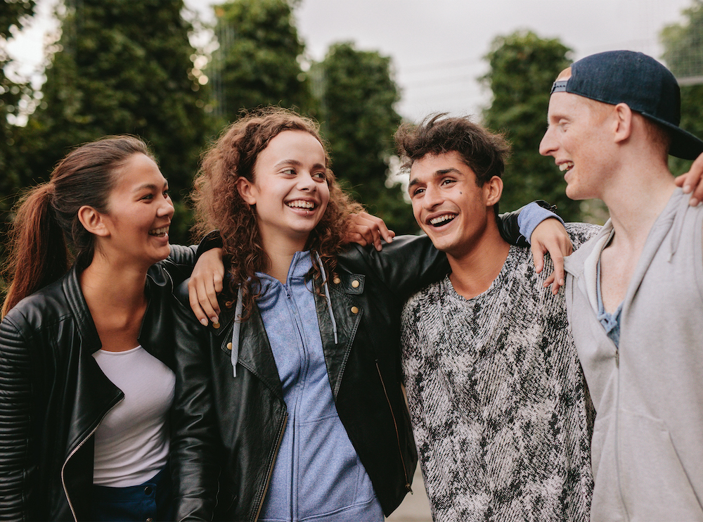 Portrait of multiracial group of people enjoying outdoors. Four young friends standing together and smiling.